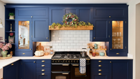 Modern kitchen shows oak beam with blue cabinets, white tiled backsplash, and black stovetop.